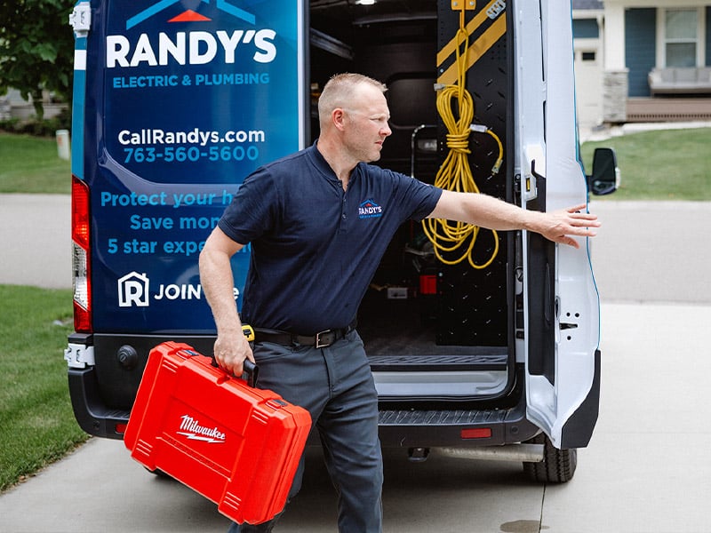 A man carrying a red toolbox near a Randy's Electric & Plumbing van.