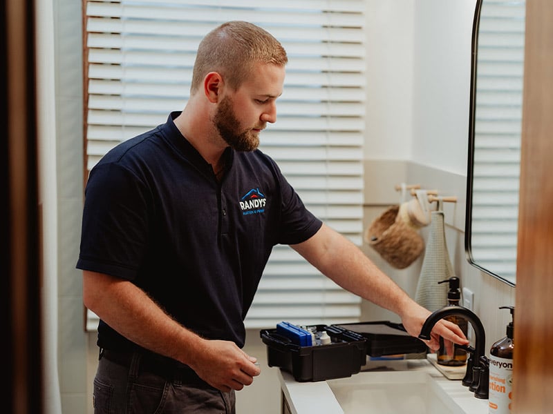 A plumber from Randy's fixing a bathroom sink faucet with tools.